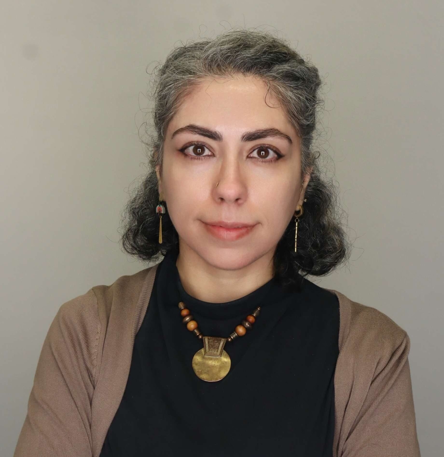 Professor Lubna Alzaroo stands looking into the camera. She wears a black shirt with a tan cardigan.