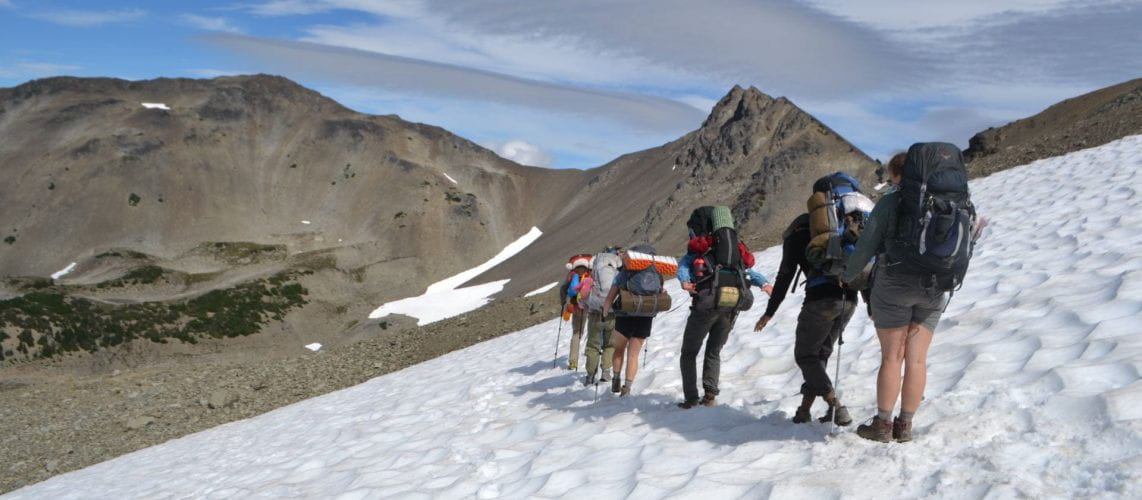 Five people standing on a snowfield in the mountains.