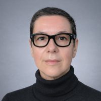 A headshot of Professor L. Monika Moskal. She wears a black turtleneck and black glasses and is against a light grey background.