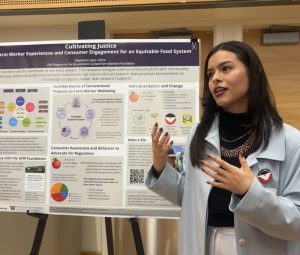 Stephanie Lopez-Jaime stands next to her capstone poster. She is mid-sentence, looking away from the camera as she talks.