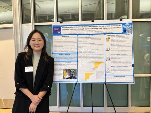 Grace Cui stands next to her capstone poster, and looks at the camera smiling. 
